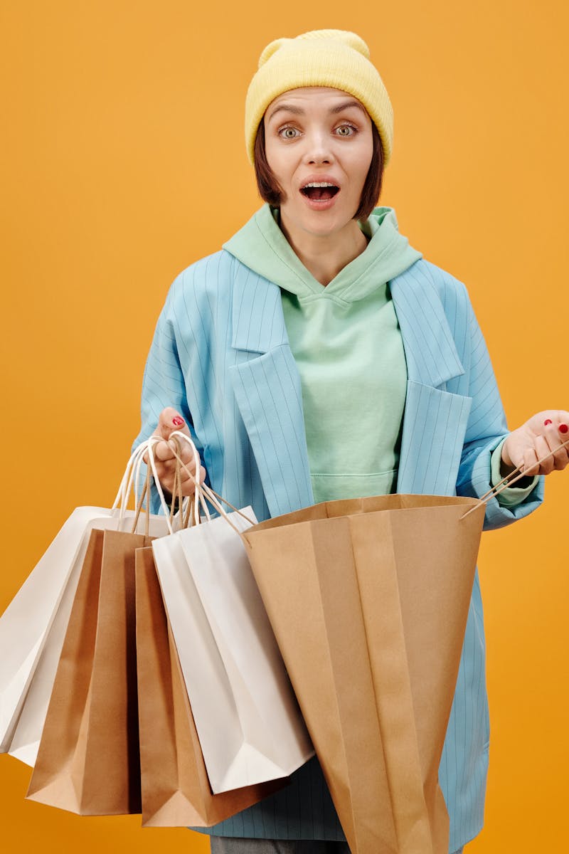 A woman in vibrant clothes holds several shopping bags against a solid background.
