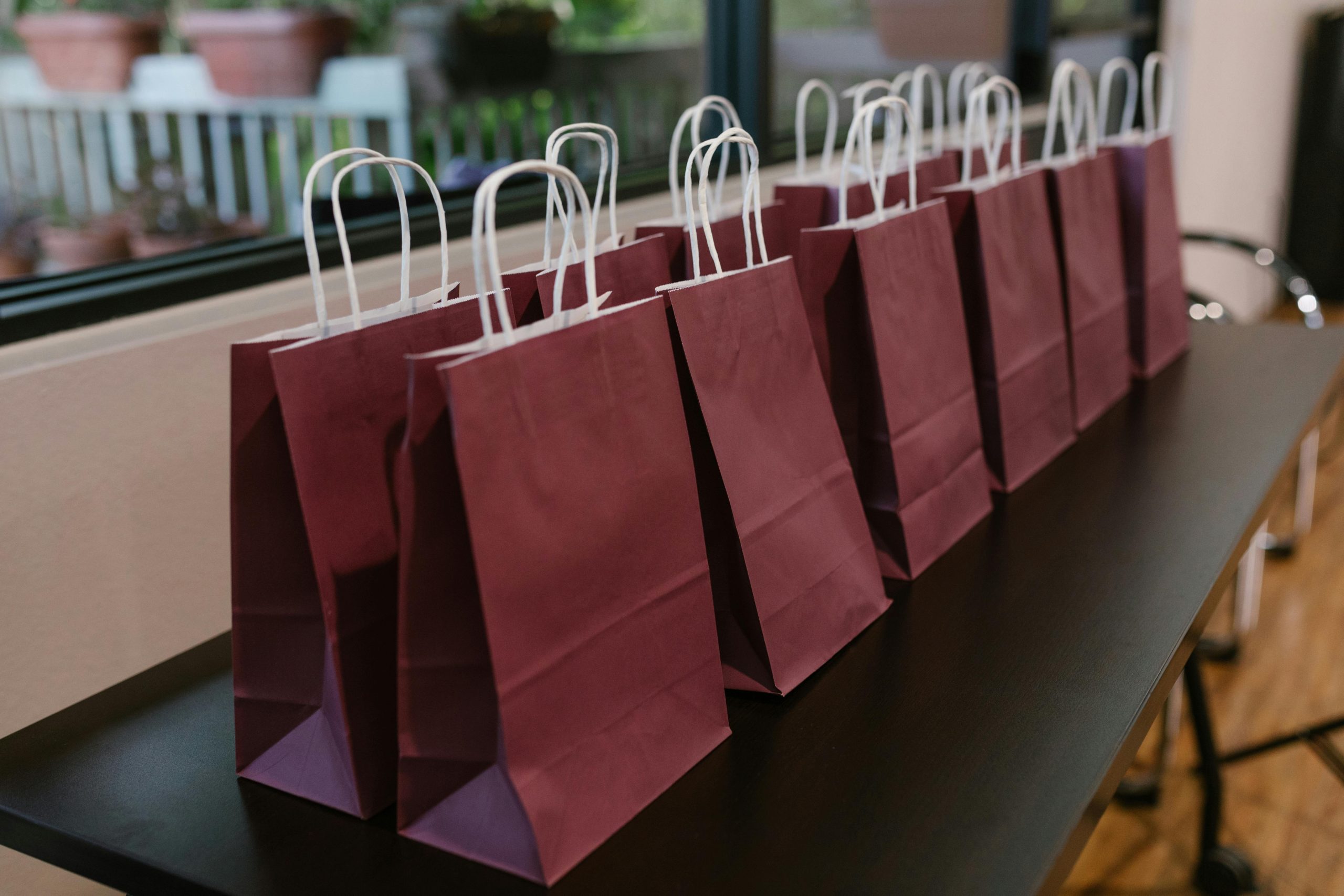 Purple paper bags with handles lined up on a table indoors, perfect for events.